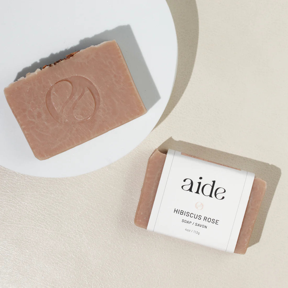 two bars of soap next to a white plate, one has a white band label with black logos and text