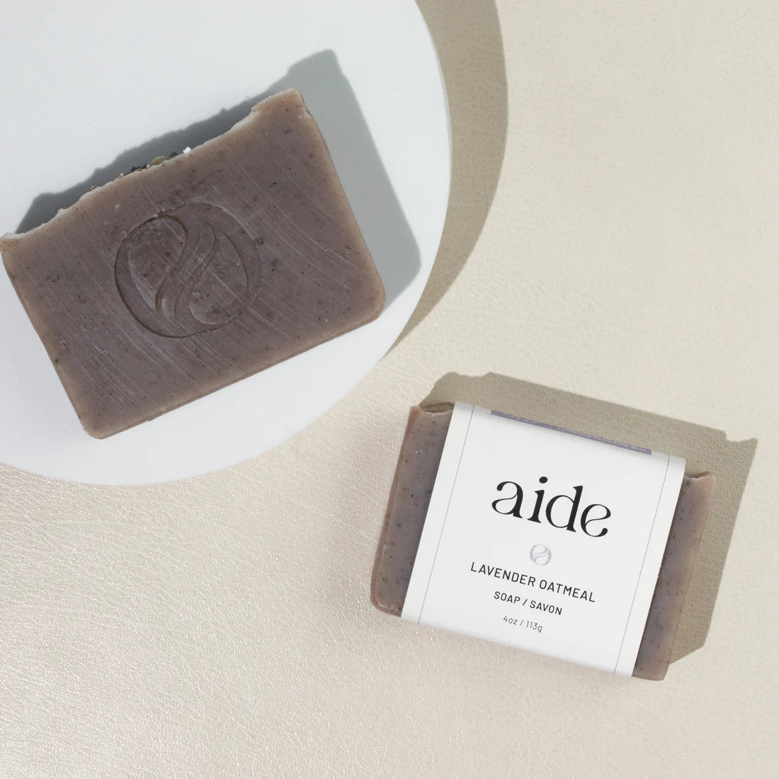 two brown bars of soap next to a white plate,  with one sporting a white band label