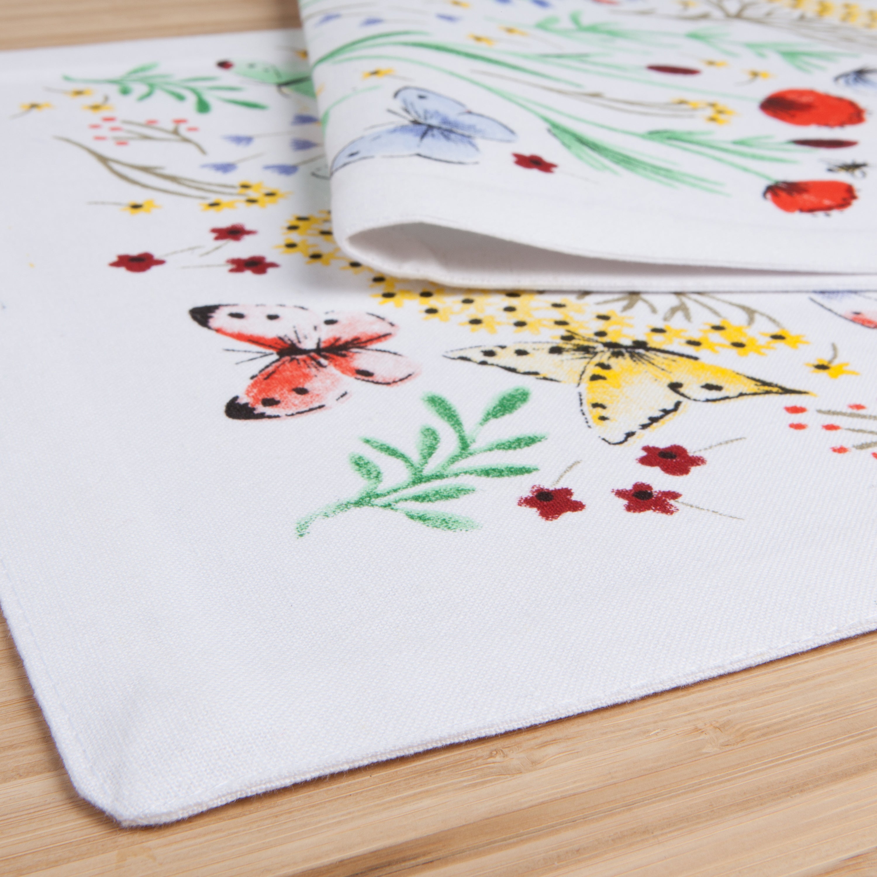  close up of an Off-white semi-folded table runner with various different types of grass, and flowers alongside different types of flowers