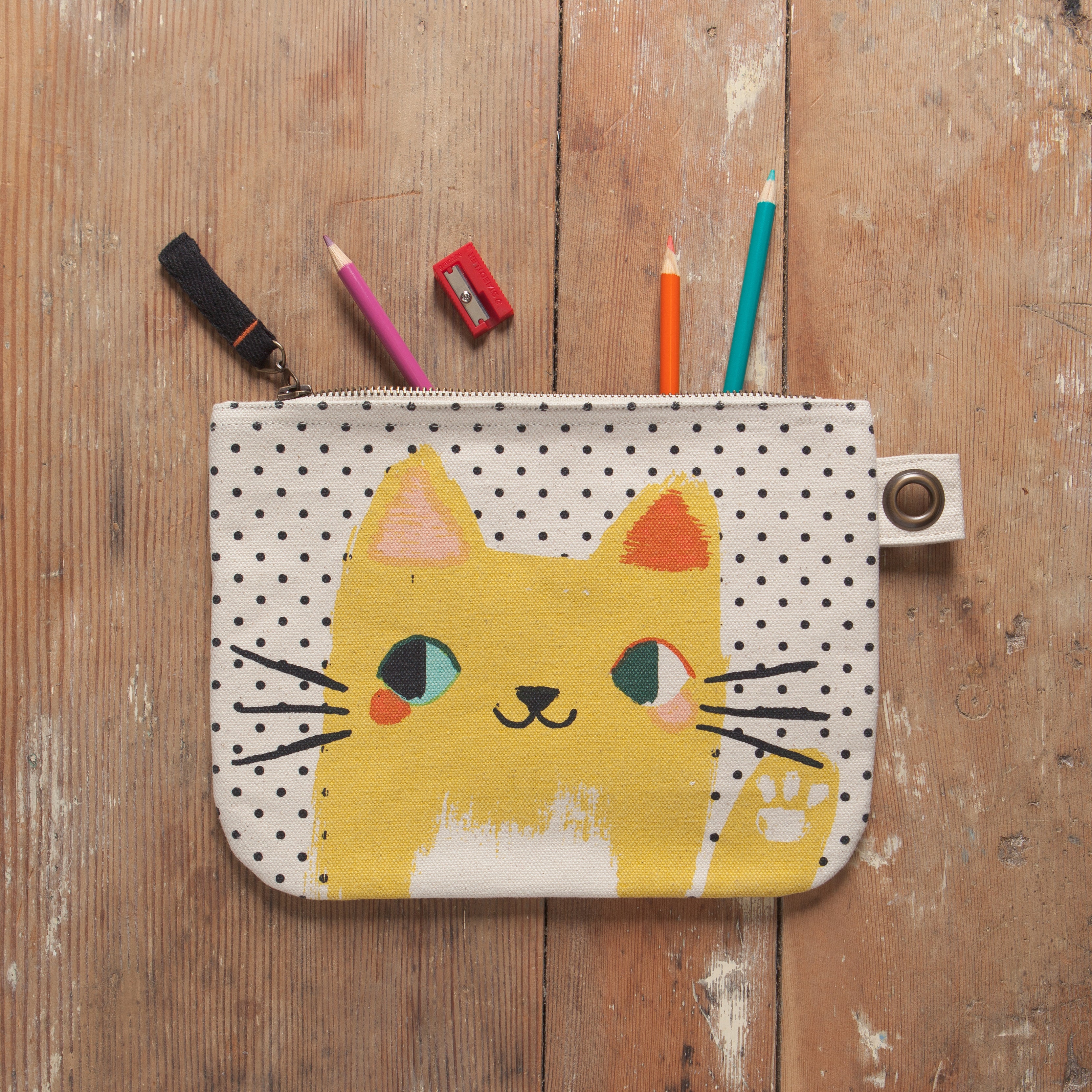 white zip up pouch with black polka dots and a yellow waving cat on a desk filled with utensils