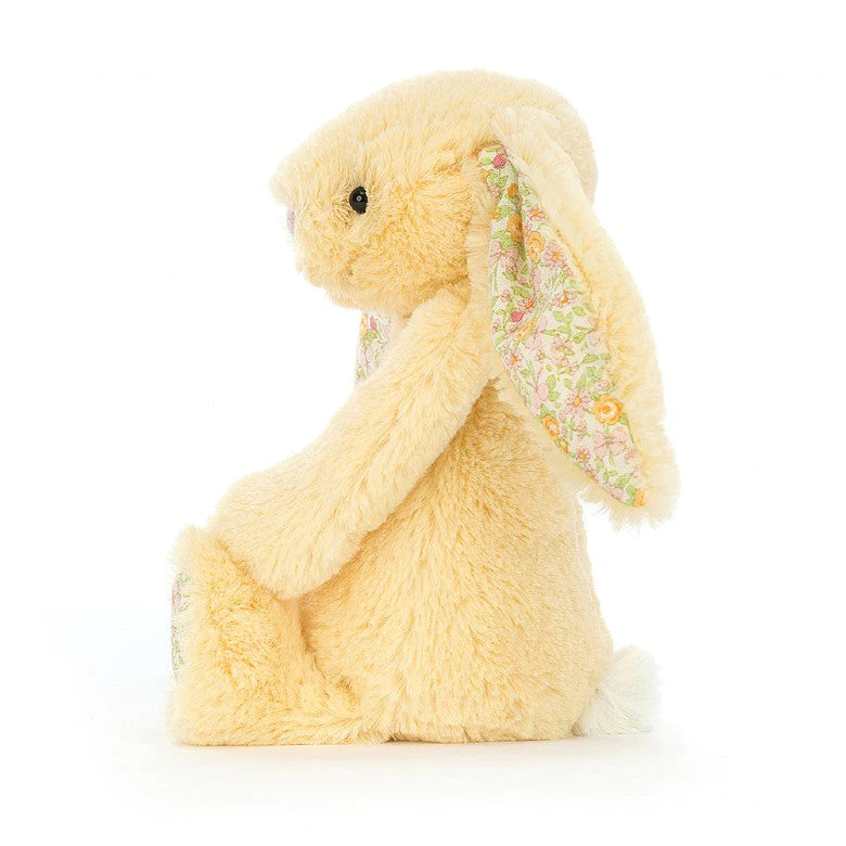 side view of a light yellow plush bunny with a yellow floral design on the bottom of the feet and the inner ears  