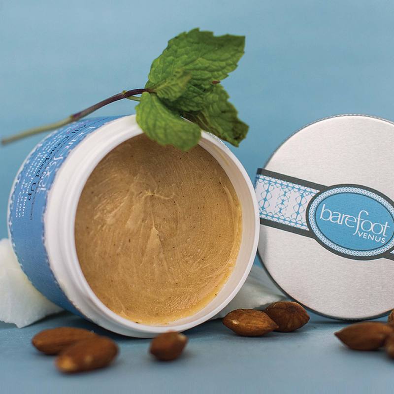 Light brown foot cream in a white jar with an intricate light blue label, almonds, and mint surrounding it