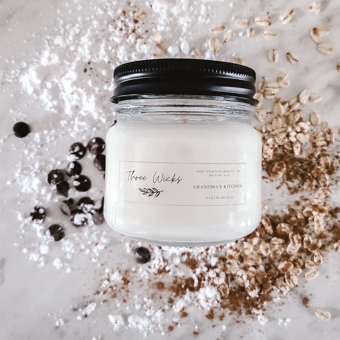 clear mason jar with a black lid and a white wax candle inside and a clear and black label that has blueberries, oats, and flour behind it