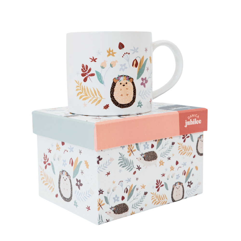 white mug with an illustrated hedgehog, surrounded by different illustrated plants sitting on top of a box with the same design