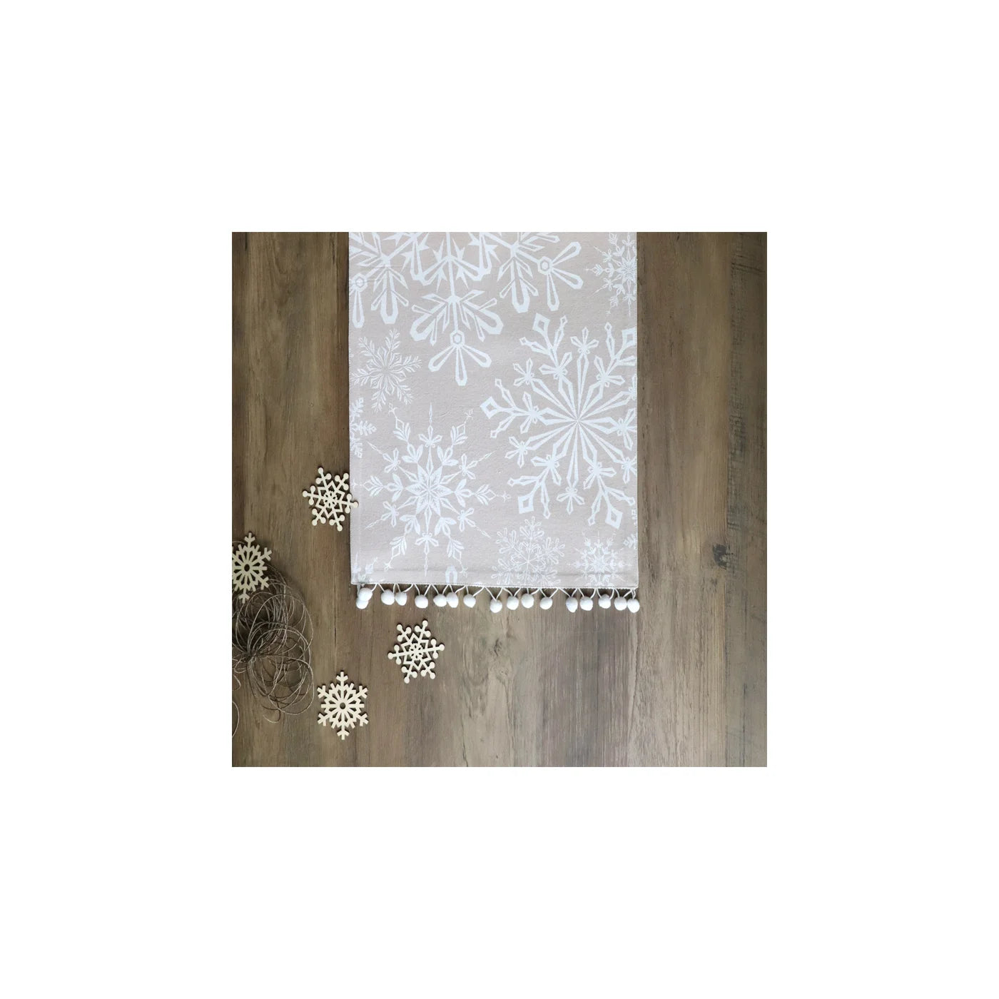 light grey table runner with a white snowflake pattern and physical white snowflake decorations in front of it 