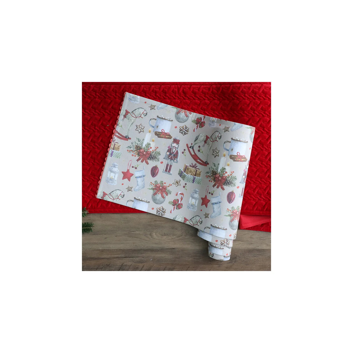 Light grey rolled up table runner with various christmas images on it, in front of a red blanket