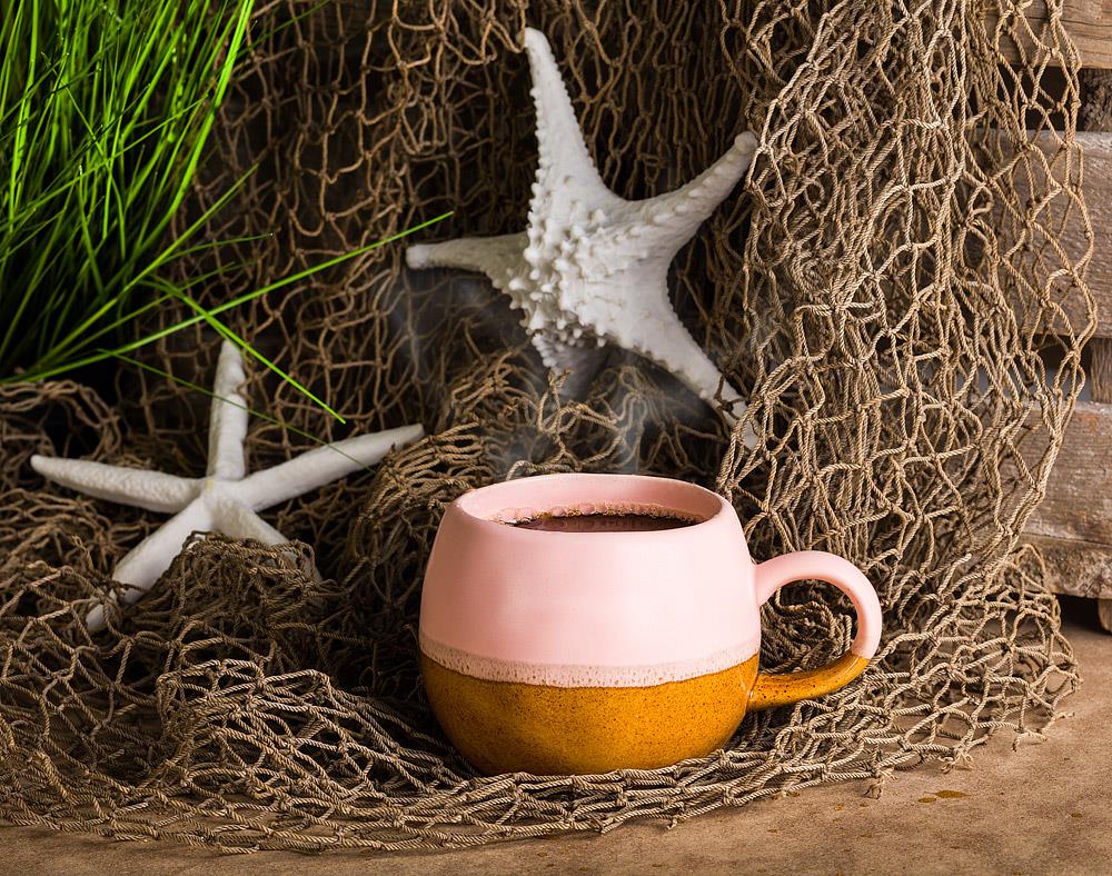Light pink and brown round textured mug next to a fishing net, sea stars, and sea weed
