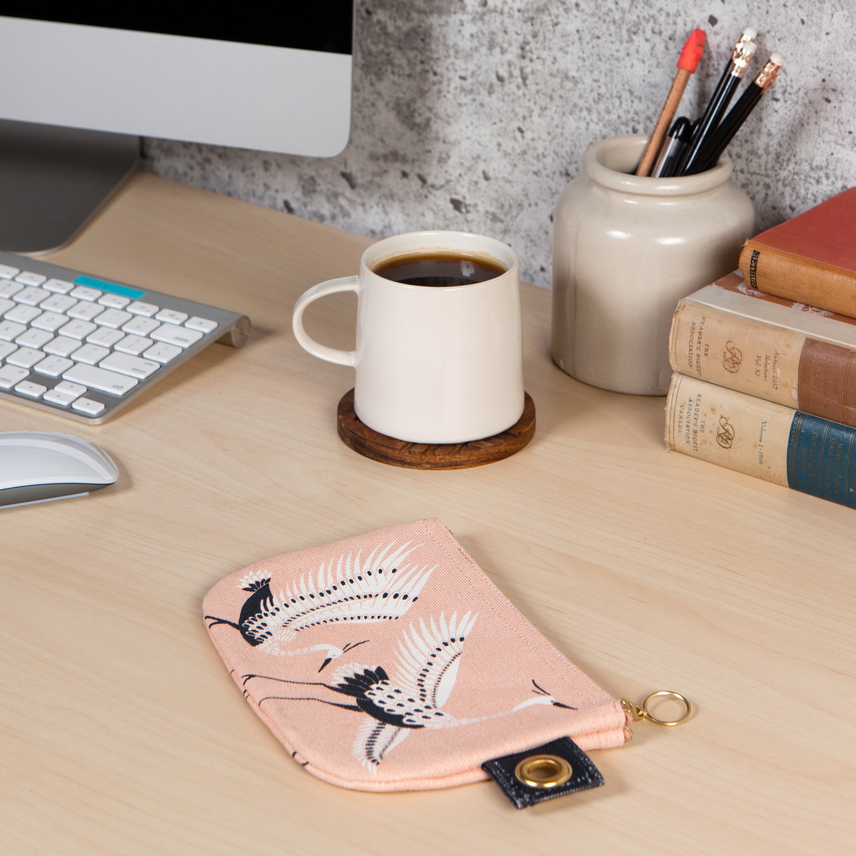 light pink zip up pouch with white and navy blue herons  on a desk beside a home computer and a cup of coffee