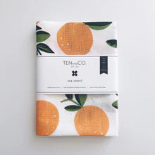 White kitchen tea towels with a pattern of oranges with green stams folded up wrapped with a ten and co logo