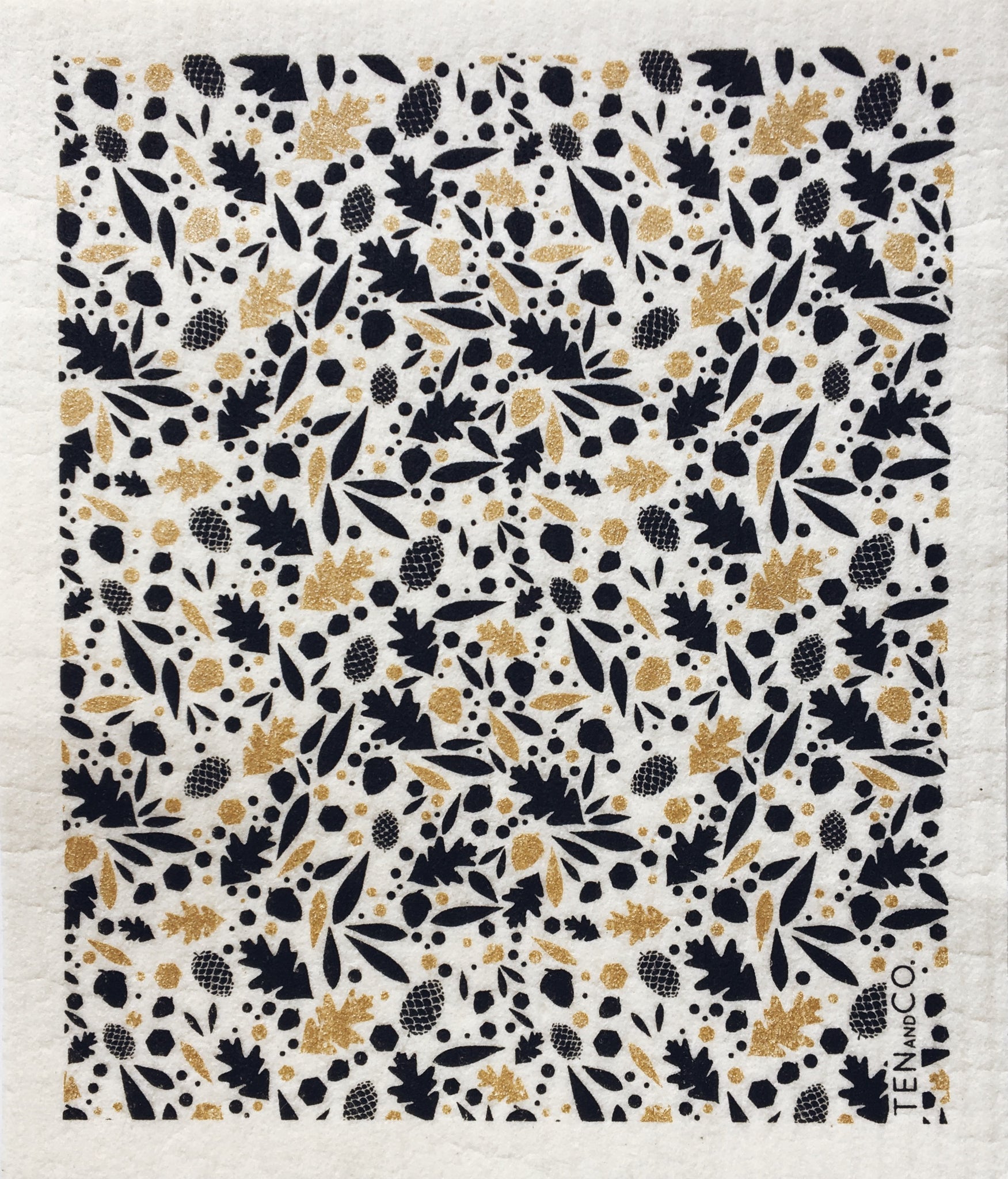 white tea towel with  gold and black oak leaves and acorns in a pattern covering the towel